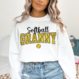 May include: White sweatshirt with the text "Softball Granny" in black lettering with a yellow softball graphic.