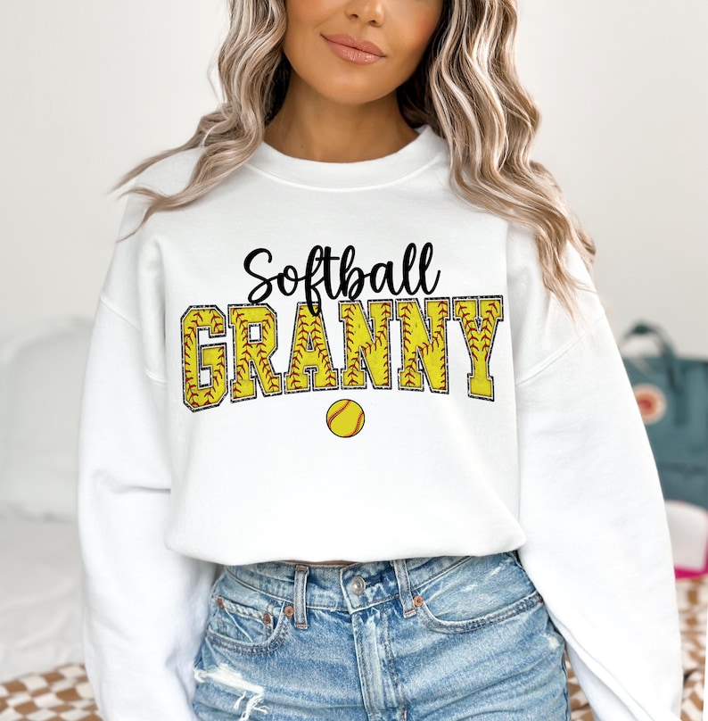 May include: White sweatshirt with the text "Softball Granny" in black lettering with a yellow softball graphic.