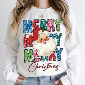 Op de afbeelding: Witte trui met een feestelijk ontwerp met de woorden "Merry Christmas" in kleurrijke glitterletters en een vintage illustratie van de kerstman.