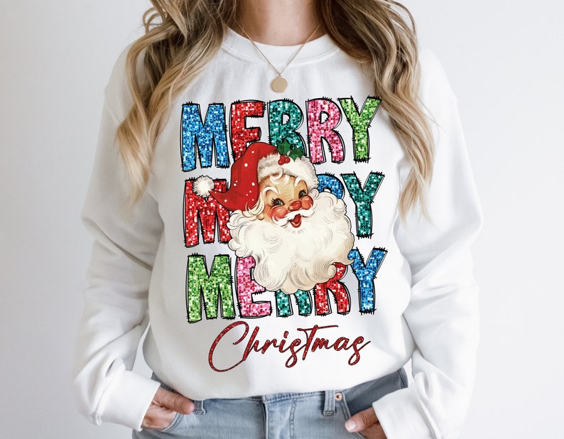 Op de afbeelding: Witte trui met een feestelijk ontwerp met de woorden "Merry Christmas" in kleurrijke glitterletters en een vintage illustratie van de kerstman.