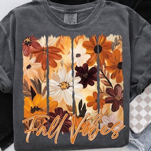 May include: Dark gray sweatshirt featuring a floral design in shades of orange, white, and burgundy. The words "Fall Vibes" are printed in orange script across the bottom of the floral design. The sweatshirt has long sleeves and a crew neck.