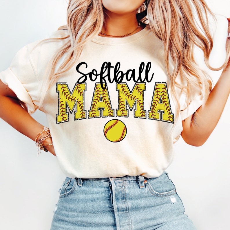May include: A white t-shirt with the text "Softball Mama" in black lettering. The letters are outlined in yellow and have a baseball stitch design. A yellow baseball is below the text.