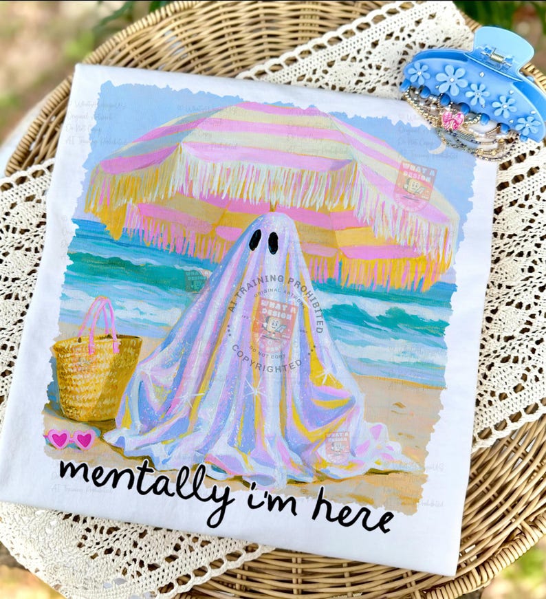 May include: A white t-shirt featuring a graphic of a ghost under a pink and yellow striped beach umbrella on a sandy beach. The design includes a straw tote bag, pink heart-shaped sunglasses, and the black text "mentally i'm here" at the bottom.