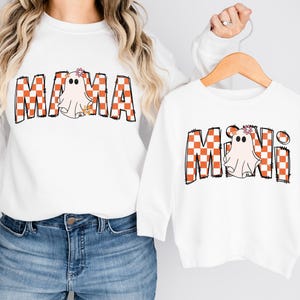 Pu&ograve; includere: Camicie bianche a maniche lunghe con fantasie di fantasmi a scacchi arancioni e bianchi. La camicia pi&ugrave; grande dice "MAMA" e quella pi&ugrave; piccola dice "MINI".