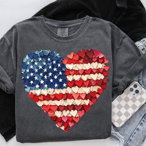 May include: A charcoal gray t-shirt with a heart-shaped design made of red, white, and blue hearts. The design resembles the American flag.