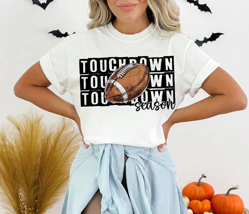 Op de afbeelding: Wit T-shirt met een zwart-witte afbeelding van een voetbal en de tekst "Touchdown season".
