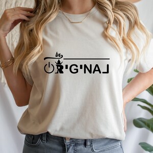 May include: A white t-shirt with black text that reads "be original" with a crown and an on/off switch graphic.
