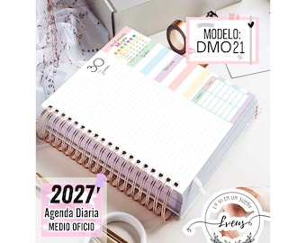 May include: A 2027 daily planner with a copper-colored spiral binding. The open page features a dotted grid layout, a small calendar for May, and pastel-colored sections for notes and expenses. Text on the page includes 30 Jueves, 2027 Agenda Diaria MEDIO OFICIO, and MODELO: DMO21.