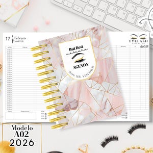Könnte beinhalten: Ein spiralgebundenes Notizbuch mit einem rosa-goldenen geometrischen Design. Auf dem Cover steht "But first mascara AGENDA DOS MIL VENTISES". Das Notizbuch enthält Abschnitte für Termine und Notizen, mit dem Datum "17 Febrero MARTES".