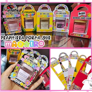 Könnte beinhalten: Bunte Geschenkboxen mit Griff, jeweils mit einem kleinen Glas Duftlotion. Die Boxen tragen das Crayola- und Pritt-Branding mit spanischem Text. Die Boxen sind mit Illustrationen zum Thema Schule und dem Text "La Mejor Maestra" verziert.