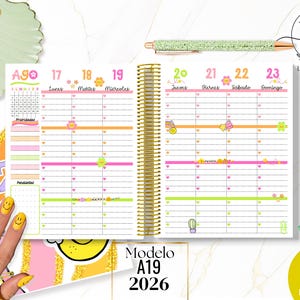 Puede incluir: Cuaderno de planificación semanal abierto en una página de agosto, con encuadernación en espiral dorada. El diseño incluye líneas coloridas, emoticonos sonrientes e ilustraciones pequeñas. El texto "Modelo A19 2026" es visible.