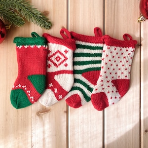 May include: Four red and white knitted Christmas stockings with different patterns. The stockings are hanging on a wooden background.