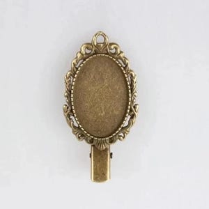 Puede incluir: Un marco de metal dorado con una abertura ovalada, perfecto para agregar un toque personal a las joyas o manualidades.