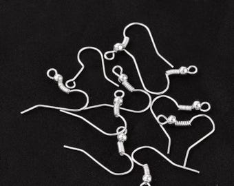 May include: A close-up of silver earring hooks with a small ball at the end of each hook. The hooks are arranged in a random pattern on a black surface.