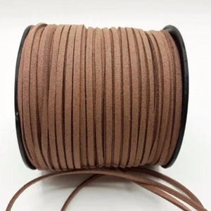 May include: A spool of brown suede cord, wound around a black plastic bobbin. The cord is approximately 3 mm wide.