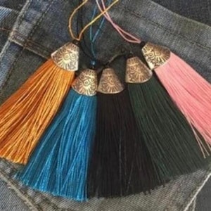 May include: Five colorful tassel keychains with decorative metal tops. The tassels are orange, teal, black, dark green, and pink.