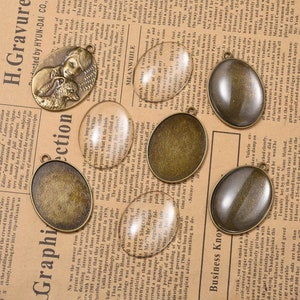 Op de afbeelding: Een verzameling ovale, antieke, bronzen, glazen, metalen fotolijstjes. De lijstjes zijn gerangschikt op een bedrukte pagina met tekst.