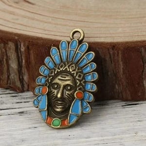 Peut inclure: Un pendentif en bronze représentant le visage d'un chef amérindien avec une coiffe bleue et orange. Le pendentif a une boucle en haut pour l'attacher à une chaîne ou un cordon.