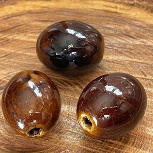 Peut inclure: Trois perles en céramique brunes avec une finition brillante. Les perles sont de forme ovale et ont un trou au centre.