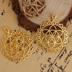 以下が含まれることがあります： 幾何学的な花のデザインが施された、金色の金属製のペンダントが2つ。ペンダントは円形で、繊細で複雑なパターンが施されています。