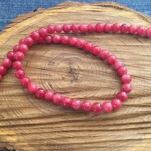 Peut inclure: Un brin de perles de pierres précieuses roses. Les perles sont rondes et lisses, et elles sont enfilées sur un fil transparent. Les perles sont disposées en cercle lâche, et elles reposent sur une surface en bois.