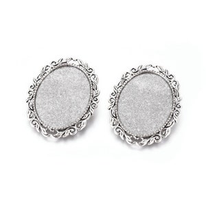 Op de afbeelding: Twee zilveren ovale blanco cameo-hangers met sierlijke bloemmotieven rond de randen.