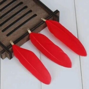 May include: Three red feathers with gold tips. The feathers are arranged in a row on a wooden surface.