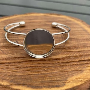 May include: A silver bangle bracelet with a round, clear glass cabochon in the center.