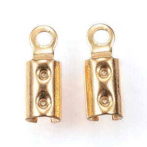 Op de afbeelding: Twee gouden metalen koord eindkappen met een kleine lus aan de bovenkant. De doppen hebben een cilindrische vorm en zijn ontworpen om de uiteinden van koorden of kettingen te beveiligen.
