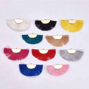 Puede incluir: Surtido de diez piezas de adorno de flecos de medio círculo de colores con detalles metálicos dorados. Cada pieza presenta un color de flecos diferente, incluyendo blanco, negro, amarillo, azul verdoso, beige, rosa, rojo, azul y gris.