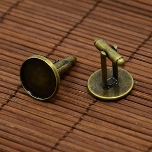 Peut inclure: Une paire de boutons de manchette en or antique avec des sertis ronds et vides. Les boutons de manchette sont en métal et ont un aspect vintage.