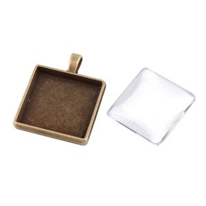 Könnte beinhalten: Ein quadratischer Anhänger-Tablett mit Bronze-Finish und einer klaren Glasabdeckung. Das Tablett hat oben eine Schlaufe zum Anbringen einer Kette.