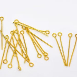 Può includere: Un gruppo di spilli per la testa dorati con un anello in cima. Gli spilli sono disposti in modo casuale su uno sfondo bianco.