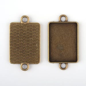 Peut inclure: Deux plateaux de pendentif en métal de couleur or antique, de forme rectangulaire et à surface texturée. Chaque plateau comporte deux boucles en haut pour attacher une chaîne ou un cordon.