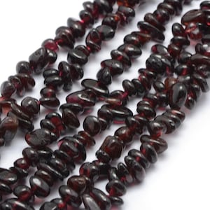 May include: A strand of dark red gemstone beads, each bead is a small, flat, irregular shape. The beads are strung together to form a long necklace.