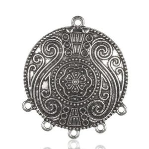 May include: Silver-toned metal pendant with a circular design featuring intricate swirls and a central flower motif. The pendant has five loops for attaching chains or cords.