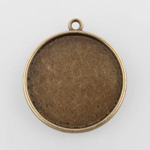 May include: A round, antique gold-toned metal pendant with a smooth, circular surface. The pendant has a loop at the top for attaching a chain or cord.