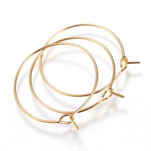 Può includere: Tre componenti per orecchini a cerchio color oro sono esposti su sfondo bianco. Ogni componente dell'orecchino ha un cerchio circolare con un piccolo perno dritto che si estende dal basso, progettato per il fissaggio a un gancio per l'orecchio.