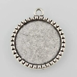 Op de afbeelding: Ronde zilverkleurige hanger met een glad, vlak oppervlak en een decoratieve rand. De hanger heeft een lus aan de bovenkant om een ​​ketting aan te bevestigen.