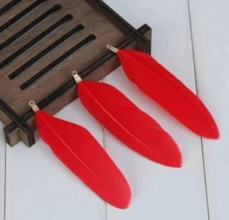 May include: Three red feathers with gold tips, arranged on a wooden surface.