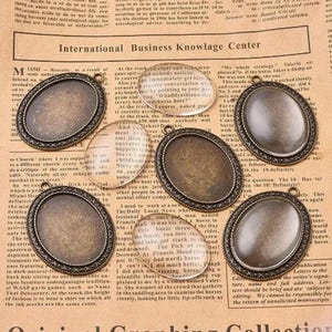 Op de afbeelding: Ovale antiek bronzen hangers met een lus om aan een ketting te bevestigen. De hangers hebben een heldere glazen inzet, ideaal voor het weergeven van foto's of kleine kunstwerken. Perfect voor het maken van sieraden en knutselen.