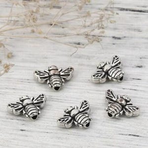 Può includere: Cinque ciondoli a forma di ape argentati con ali e corpi dettagliati. I ciondoli sono perfetti per la creazione di gioielli, lo scrapbooking e altri progetti di artigianato.