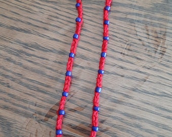May include: Red cord necklace with blue beads and a wooden cross pendant. The necklace is knotted and features small blue beads spaced along the red cord. The cross is a light brown color and has a simple, classic design.