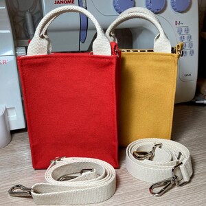 May include: Two small canvas tote bags with white straps and a detachable strap. The bag on the left is red and the bag on the right is yellow.