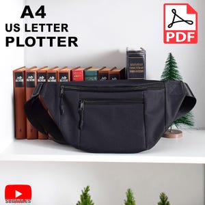 以下が含まれることがあります： 2つのジッパー付きポケットと調節可能なストラップが付いた黒いファニーパック。ファニーパックは、本と小さな鉢植えの木のある棚の上に置かれています。