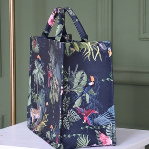 Op de afbeelding: Een zwarte tote bag met een tropische print met toekans, papegaaien en junglebegroeiing.