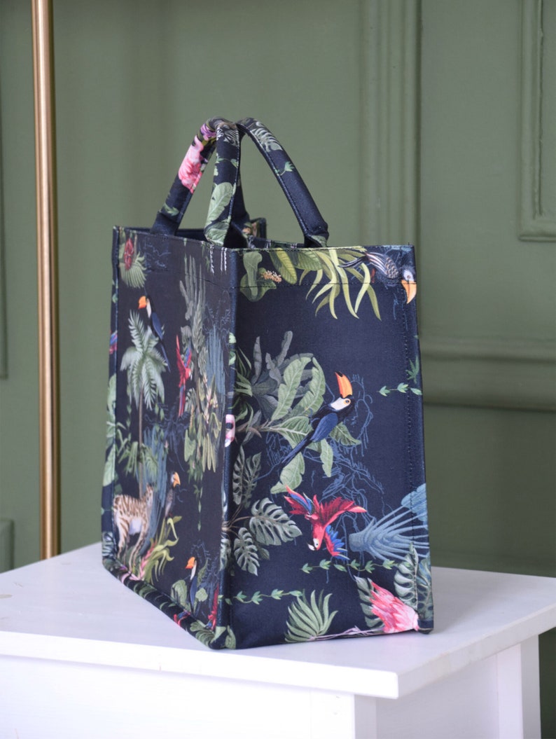 Op de afbeelding: Een zwarte tote bag met een tropische print met toekans, papegaaien en junglebegroeiing.