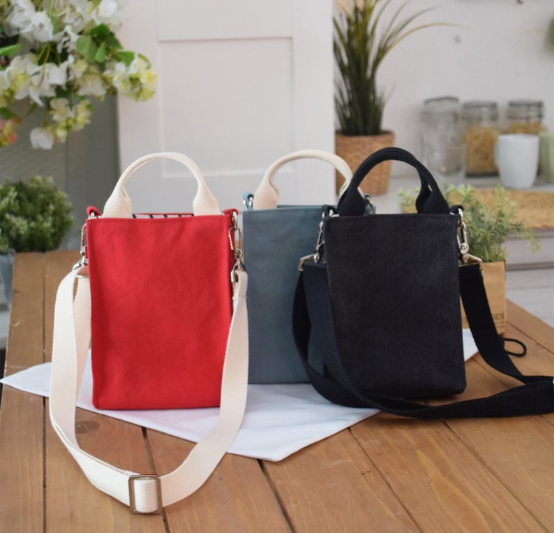 May include: Three small canvas tote bags with adjustable straps. The bags are red, blue, and black.