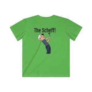 Puede incluir: Una camiseta verde con un dibujo animado de un golfista balanceando un palo de golf. El texto "The Scheff!" está impreso en la parte posterior de la camiseta.