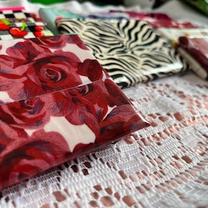 May include: A collection of rectangular wallets crafted from adhesive tape, featuring various patterns including a prominent red rose floral print, a black and white zebra stripe design, and a checkered pattern with red cherry accents.